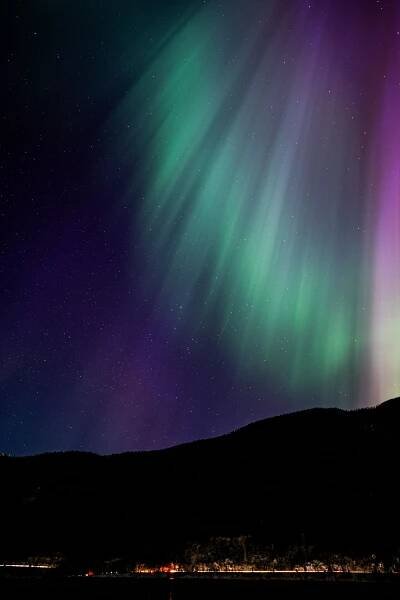 Vibrant green and purple aurora borealis lights dance across the night sky over mountain silhouettes.
