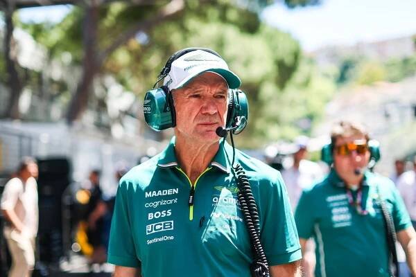 Adrian Newey is standing outside. He wears a teal polo shirt and matching headphones over a white baseball cap.