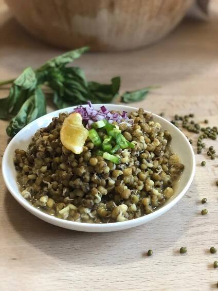 a dish with sprouted mung beans and mustard seeds topped with green chillies, purple onions, and a slice of fresh lemon.
