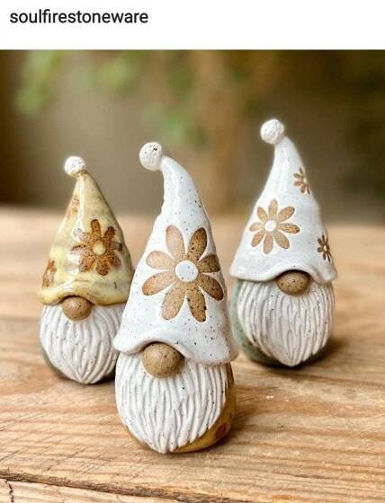 three small gnomes sitting on top of a wooden table next to each other and one is wearing a flowered hat