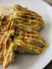 Grilled mango chicken drizzled with mango sauce and garnished with minced jalapeño on a plate.