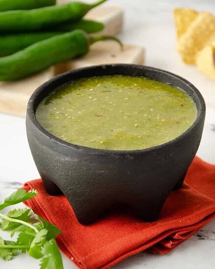 A molcajete filled with salsa verde on a bright orange napkin.