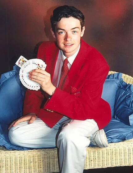Young Stephen Mulhern in a red jacket, performing a card trick.