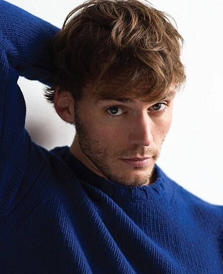 a close up of a person wearing a blue sweater with his hand on his head