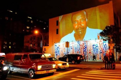 Passersby walk under a projection that is part of the non-profit organization Invisible Children's "Kony 2012" viral video campaign, in New York