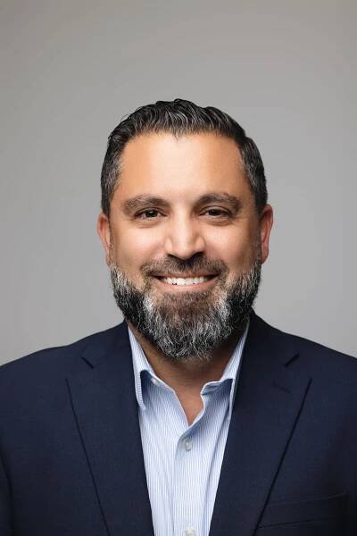 Business portrait showing person in navy blazer and light blue shirt against gray background.