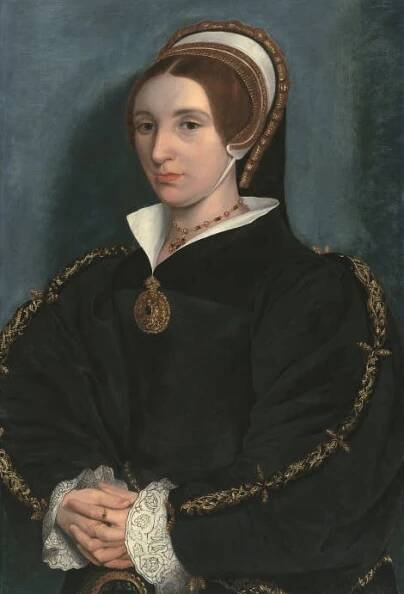 Portrait of a woman facing forward with a hat and necklace wearing a large jumper-like top with long sleeves.