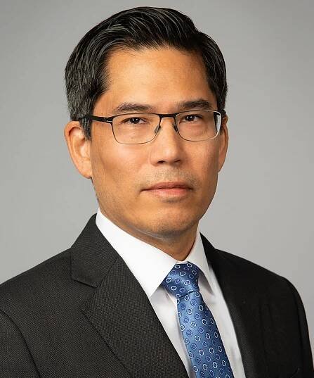 Portrait of Professor Hiro Aragaki dressed in a suit and tie, looking directly at the camera against a neutral background.