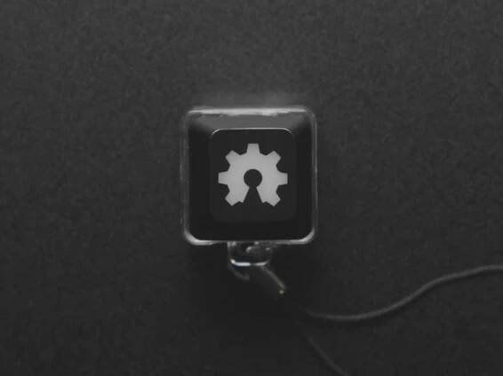 A Black woman's finger presses a keyswitch keychain. A green LED shines beneath an open source hardware logo keycap.