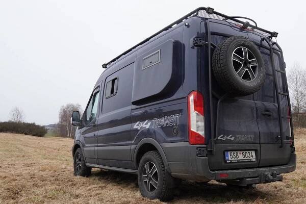Obytný Ford Transit 4x4 - pohled zezadu, na boční rozšíření, držák rezervy a žebřík.