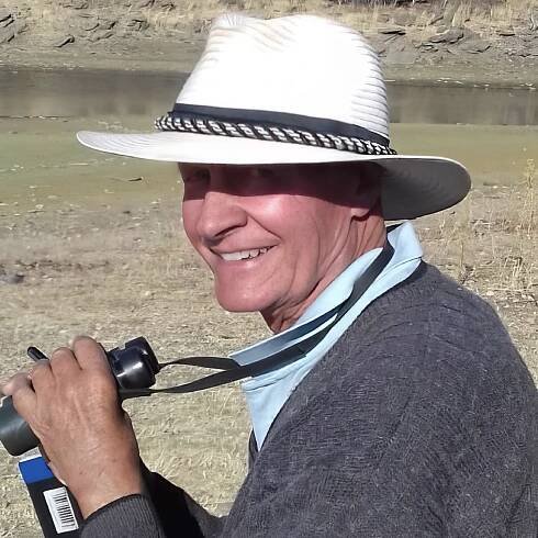 Dave Ward clutching binoculars and notebook while smiling at the camera.