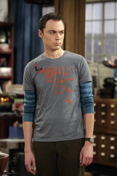 the young man is standing in his living room wearing a t - shirt with an orange bird on it