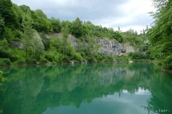 Zelené jazero obklopené stromami a skalami.
