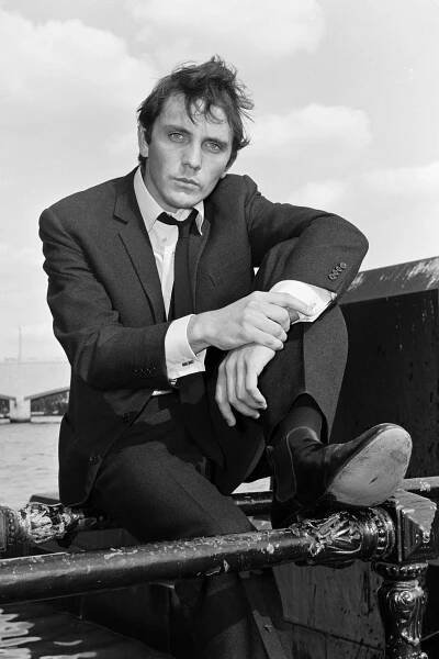 Terence Stamp, wearing a suit, poses next to a river in this black and white portrait.