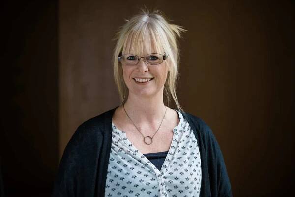 Headshot of Rachel King, a woman in glasses, a white top, dark cardigan and necklace