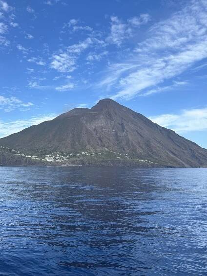 Pohled na sopku Stromboli z moře s modrou oblohou a vodní hladinou.