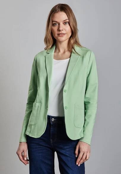 Světlý zelený blazer s klopovým límcem, dvěma předními kapsami a uzavíráním na knoflík, spárovaný s bílým topem a tmavými džíny. Hladká textura.