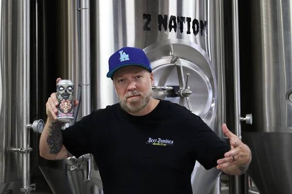 Beer Zombies Brewery owner and founder Chris Jacobs poses in front of a distillery.