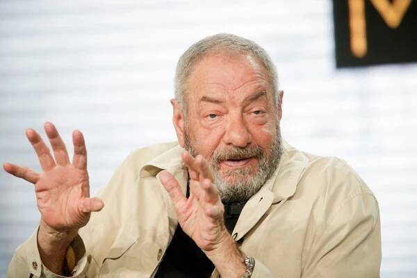 Producer Dick Wolf, wearing a black shirt and tan button down, gestures with his hands while speaking.