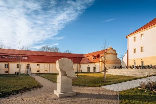 Zahrady historického kláštera v Mělníku, které jsou součástí domova pro seniory Senlife. Prostor zahrnuje sochy, lavičky a klidné prostředí.