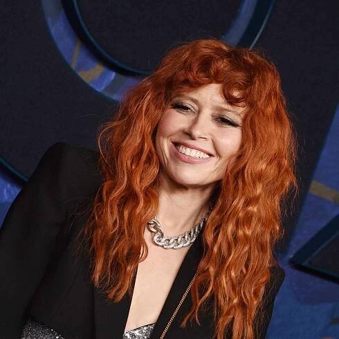 Natasha Lyonne smiling with red curly hair, bangs, boho vibes