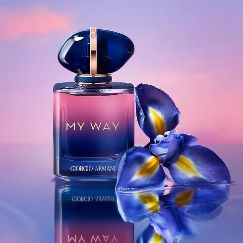 Flakon parfému Giorgio Armani My Way s modrým víčkem a zlatým nápisem stojí vedle modrého květu na lesklém povrchu, odrážející se v jemném světle.