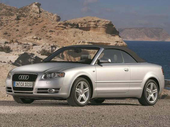 Silbernes Audi Cabriolet mit schwarzem Verdeck parkt in einer felsigen, küstennahen Landschaft unter klarem Himmel.