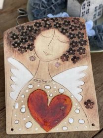 a wooden plaque with an angel holding a red heart on it's side and flowers in the background