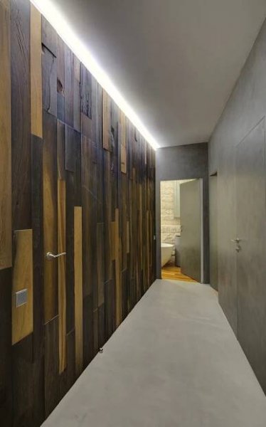 Pocit tepla s designovým efektem dodávají prostoru dřevěné obklady stěn, které architektky nechaly nainstalovat do chodby. Tvoří zajímavý kontrast s betonovou stěrkou, aplikovanou na opačné straně.