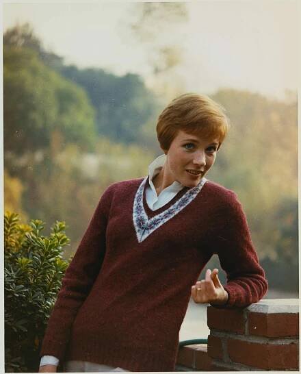 Julie Andrews outdoors leaning on a brick structure