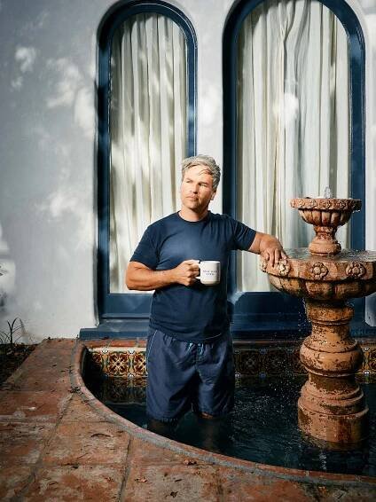 Photo: A man with gray hair wearing a blue tshirt, holding a coffee mug, and standing inside a fountain