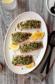 overhead view of furikake salmon fillets on a white platter with lemon wedges and black serving utenils.