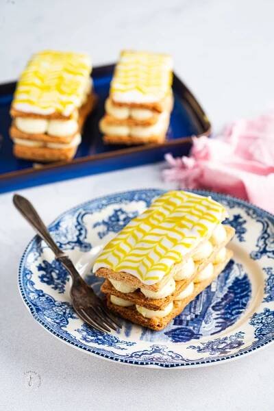 Eggless mille feuille with white chocolate saffron yogurt served in a round vintage plate with a fork.