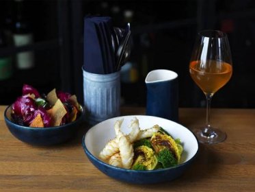 A fish and vegetable dish in blue and white bowls with a glass of bear and cultery positioned to the rear of the image