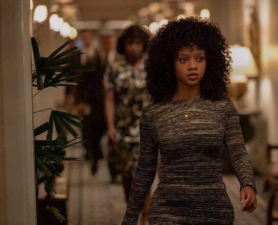 A woman with curly hair is walking down a hallway.