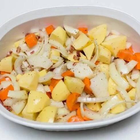 Seasoned veggies and bacon spread on the bottom of a ceramic baking dish