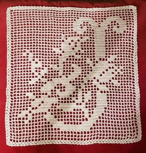 a white crocheted square on a red background with the words love written across it