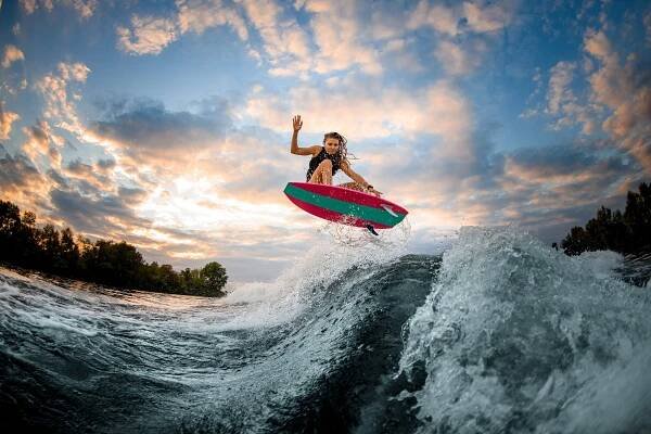 woman jumping over big splashing wave on surf style wakeboard