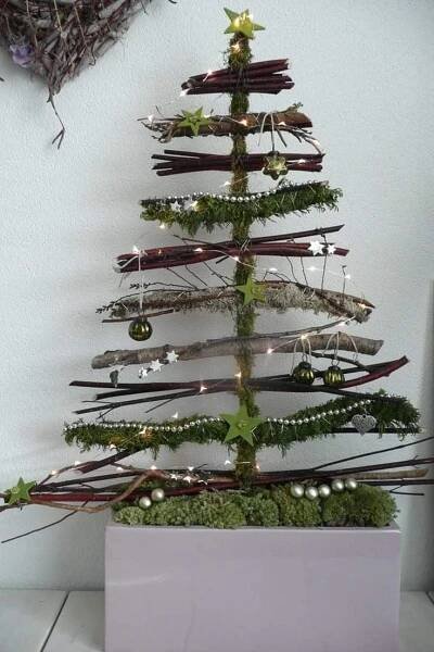 a small christmas tree made out of branches and twigs with lights on the top is sitting in a white box