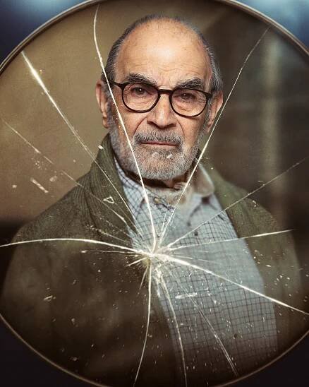 David Suchet as George, seen through cracked glass.