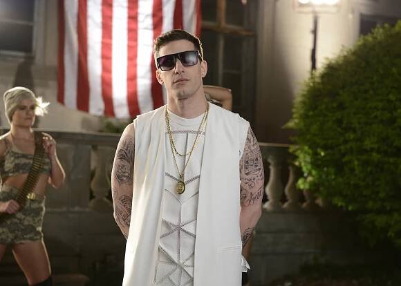 Andy Samberg in a white vest and sunglasses during a Saturday Night Live sketch.
