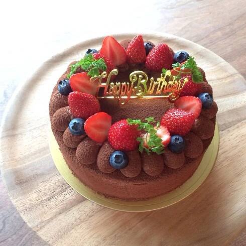 a chocolate birthday cake with strawberries and blueberries on the top sits on a wooden table