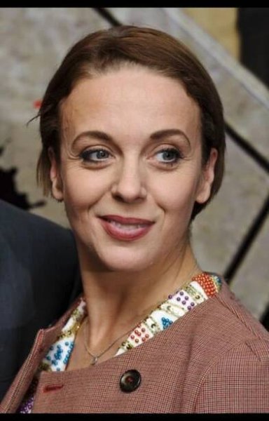 a woman with brown hair and blue eyes smiles at the camera while standing next to a man in a suit