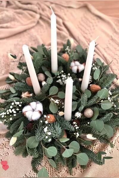 candles are arranged in a wreath with greenery and cotton balls on the tablecloth
