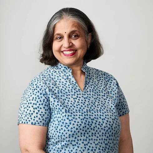 Professional headshot of a woman with short hair, wearing a blue patterned shirt, smiling warmly against a light gray background.