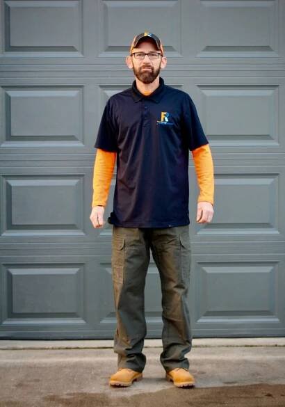 A man with a beard and glasses is standing in front of a garage door.