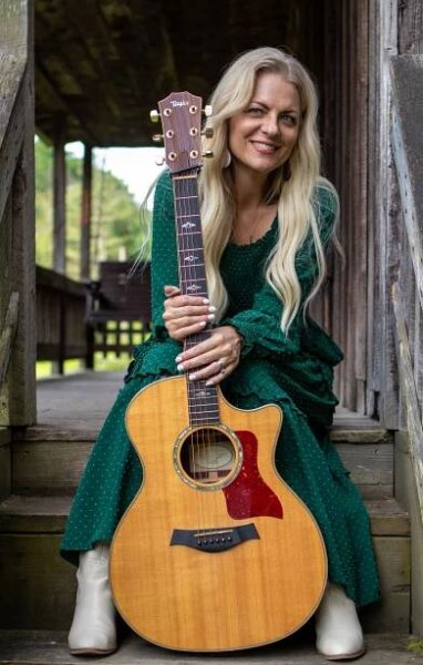 A woman in a green dress is sitting on a porch holding an acoustic guitar.
