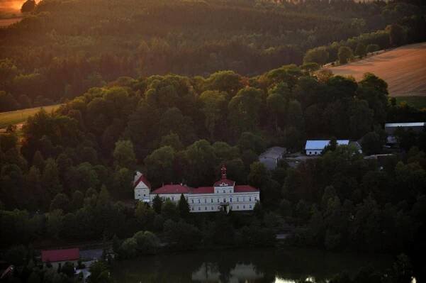 a large white building with a red roof next to a lake at Penzion Zámek Rozsochatec in Rozsochatec