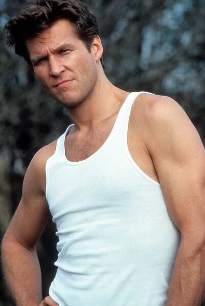 a man in white tank top holding a tennis racket and looking at the camera