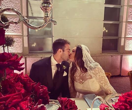 a bride and groom kissing in front of red roses